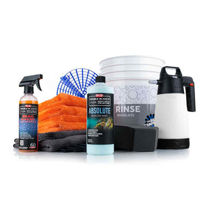 A collection of car detailing products and tools, including a bottle of Absolute Rinseless Wash and Bead Maker spray from the P&S Double Black Collection. The set also features a white rinse bucket with a grit guard, a black foam sponge, a white IK sprayer, and several microfiber towels in orange and gray. The items are arranged against a white background, showcasing a complete rinseless wash kit.