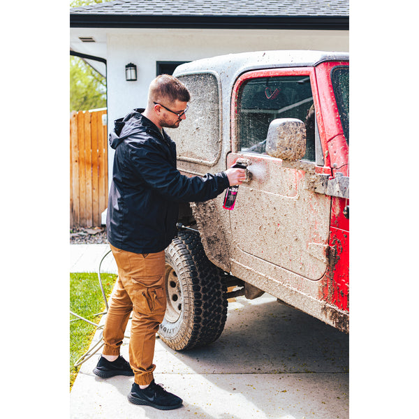 A person spraying a red jeep covered in mud with P&S Mud Buster.