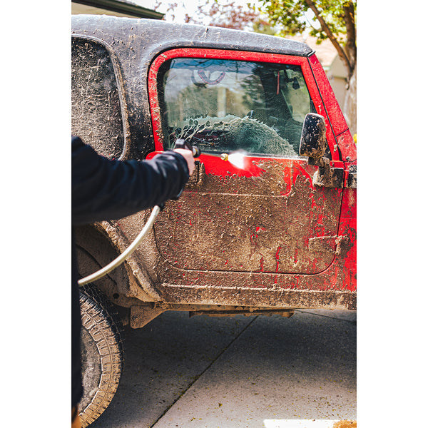 A closeup of a person spraying a muddy red jeep with a power washer.