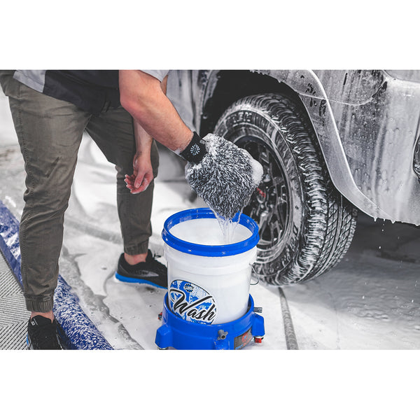 A person wearing The Rag Company Ultra Wash Mitt over a white bucket with a truck covered in foam in the background.