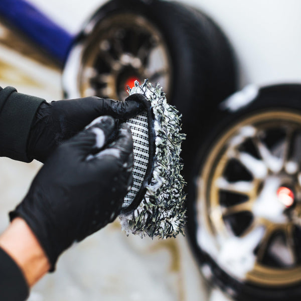 A closeup of a person putting on the Ultra Wheel Mitt with a background of two blurred tires.